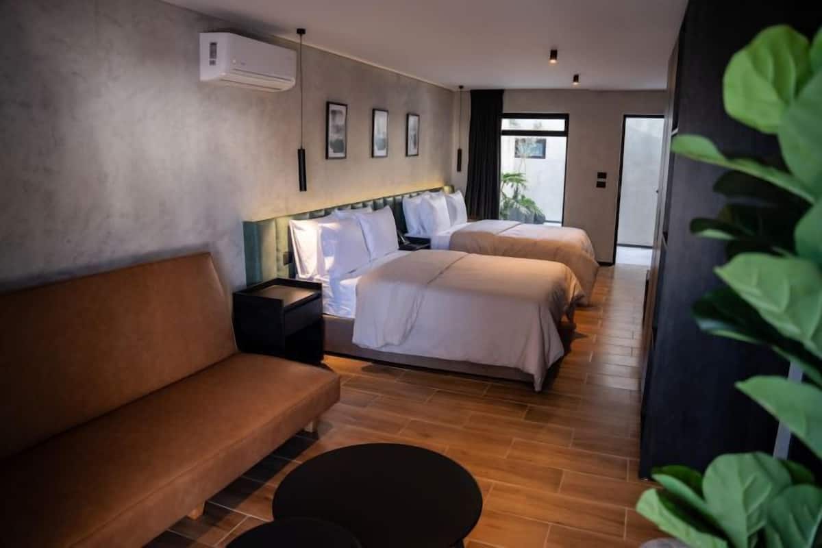 A hotel room with a sofa, two beds, a nightstand, and a small table.