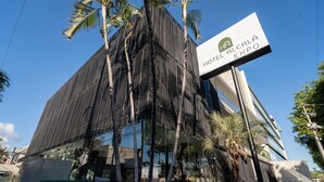 A modern building with a reflective glass facade, palm trees, and a sign for Hotel Alcalá Expo. - Hotel Alcalá Expo (Guadalajara)