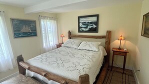 A neatly arranged bedroom with a wooden bed frame, a bedside table with a lamp, and a painting on the wall. - Charming Newly-Renovated Waterfront Cottage in Lubec (Lubec)