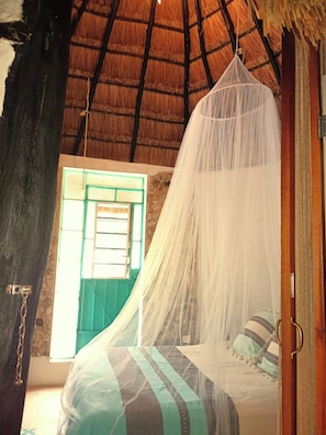 A room with a bed under a mosquito net, a window with a green door, and a thatched roof. - Hotel y Museo Aldea Maya Toktli Orígenes (Izamal)
