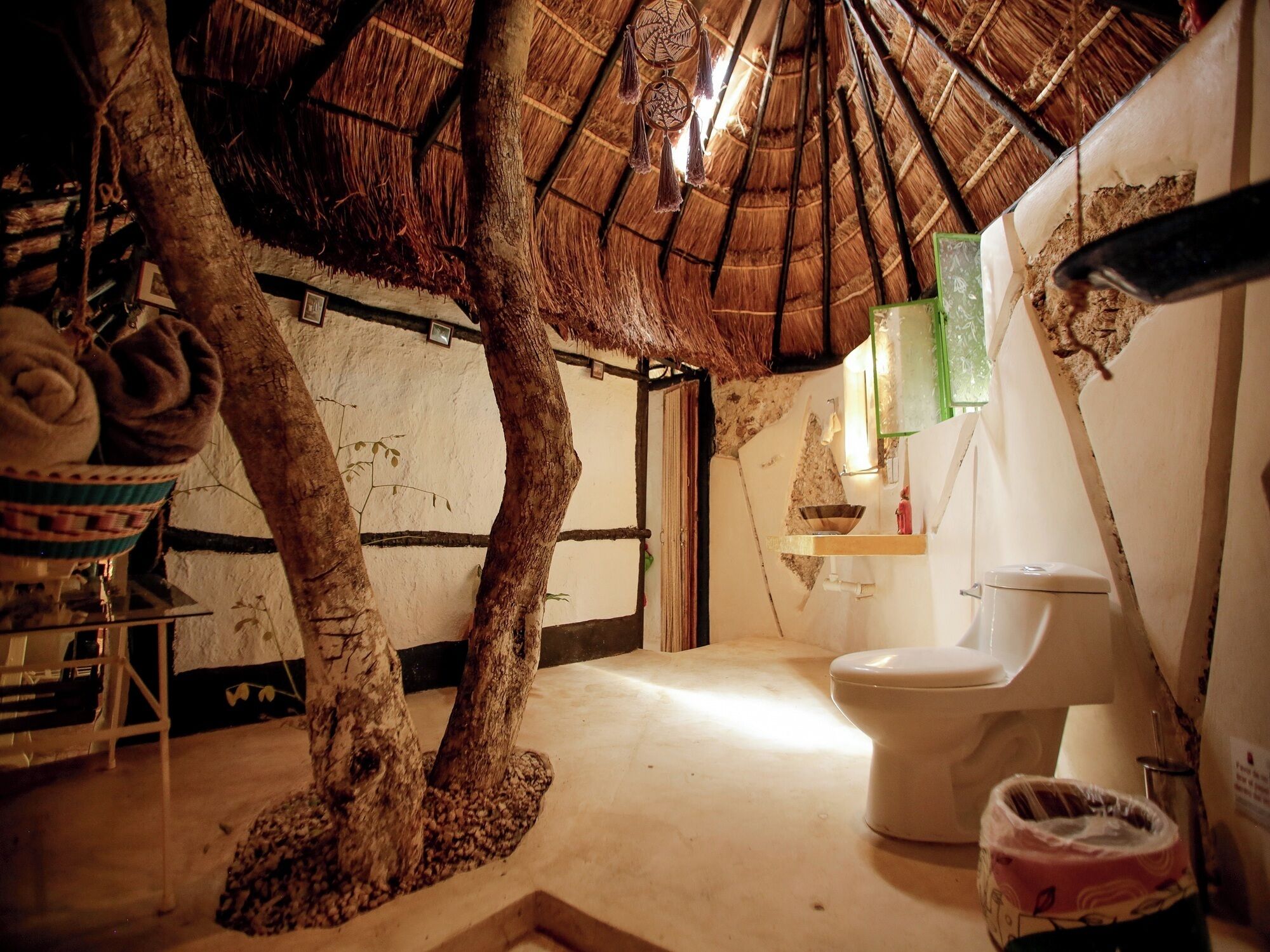 Un bagno rustico con un tronco d'albero come elemento centrale, un tetto in paglia e un semplice water.