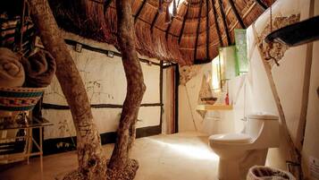 Un bagno rustico con un tronco d'albero come elemento centrale, un tetto in paglia e un semplice water.