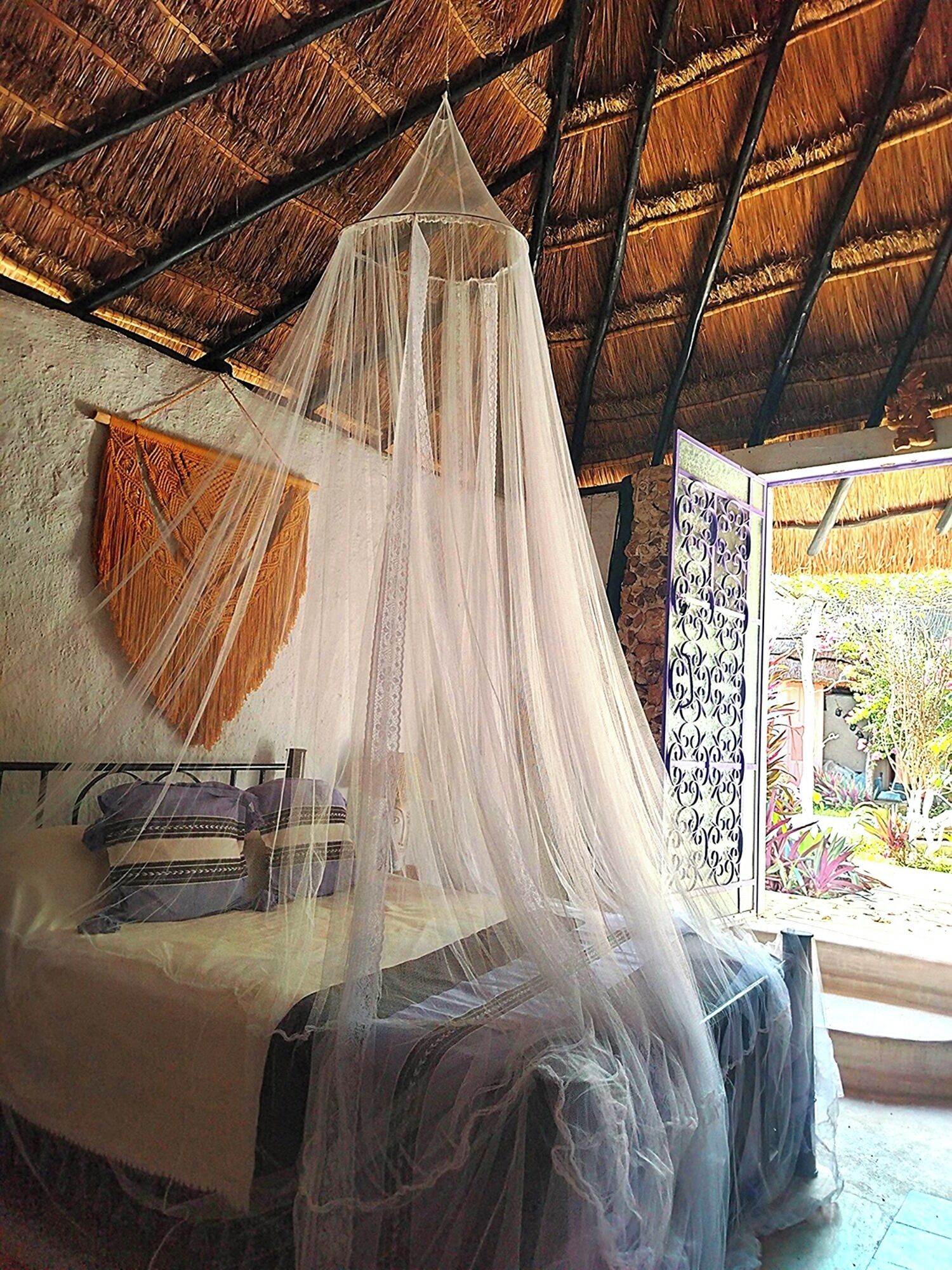 Una cama con dosel, techo de paja y vistas a un jardín.