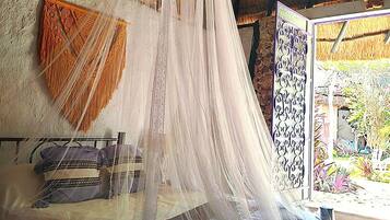 Una cama con dosel, techo de paja y vistas a un jardín.