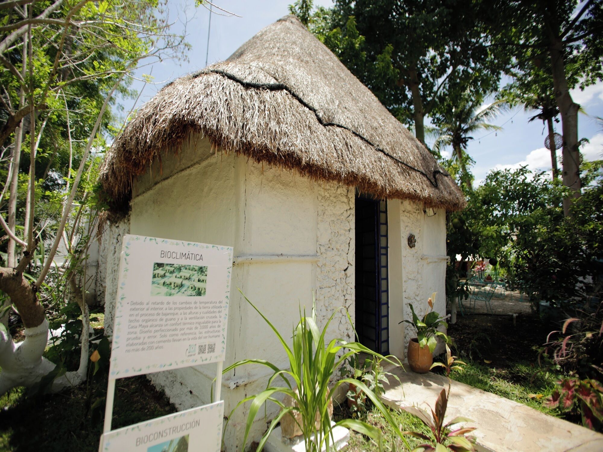 Una pequeña estructura con techo de paja, con un letrero, rodeada de vegetación.
