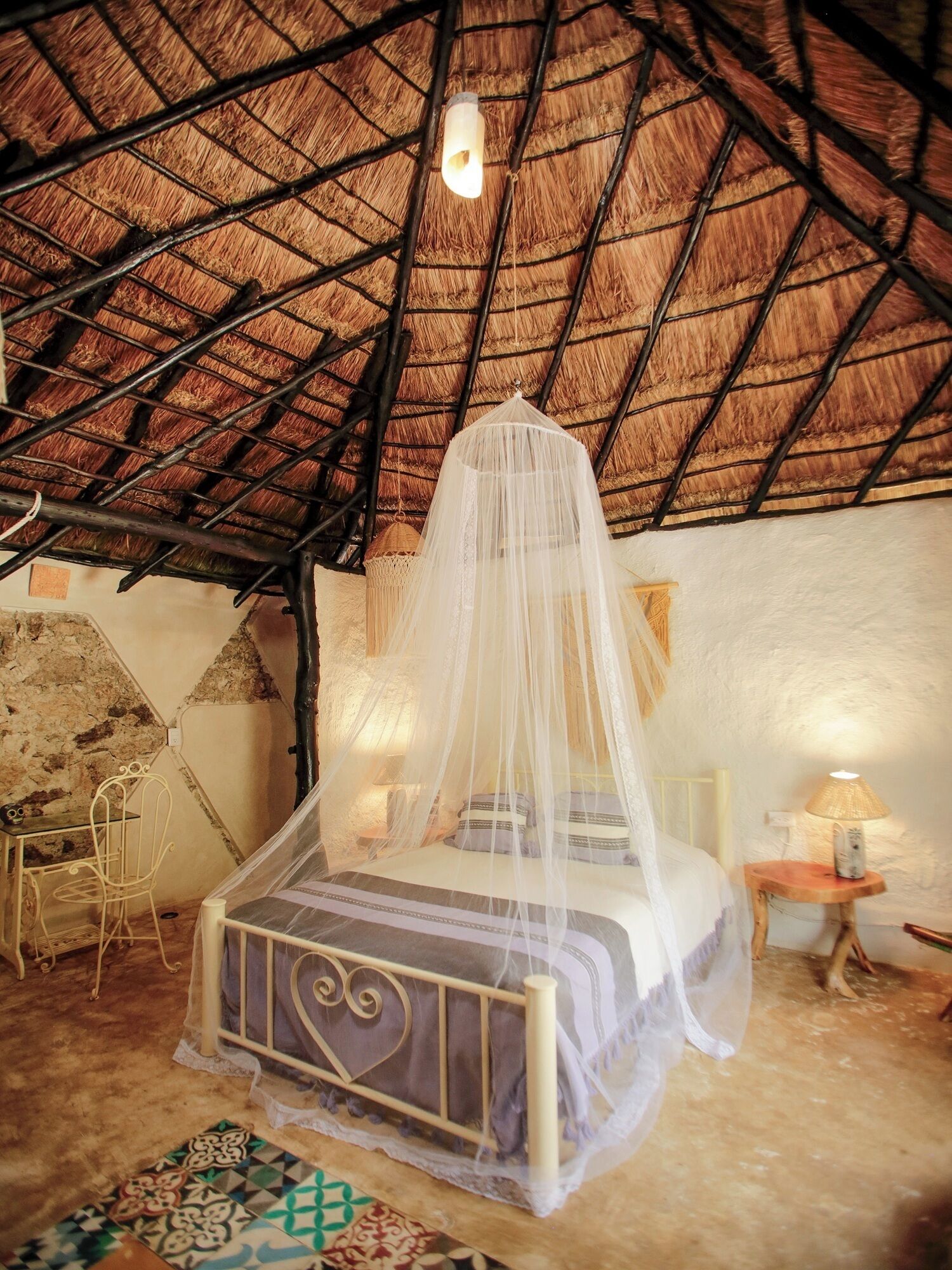 Una habitación con techo de paja, una cama con dosel, una mesita y una silla.