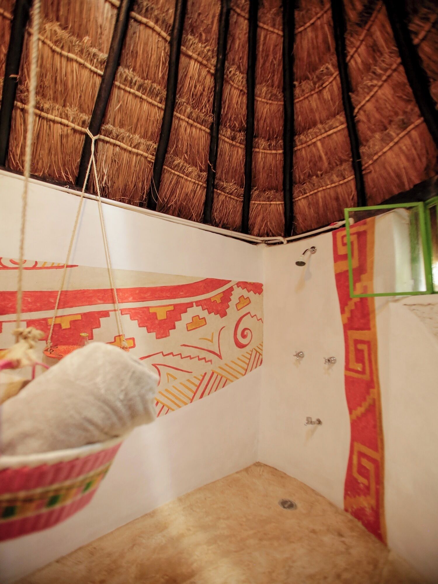 A room with a thatched roof, a hanging chair, and patterned wall decorations.