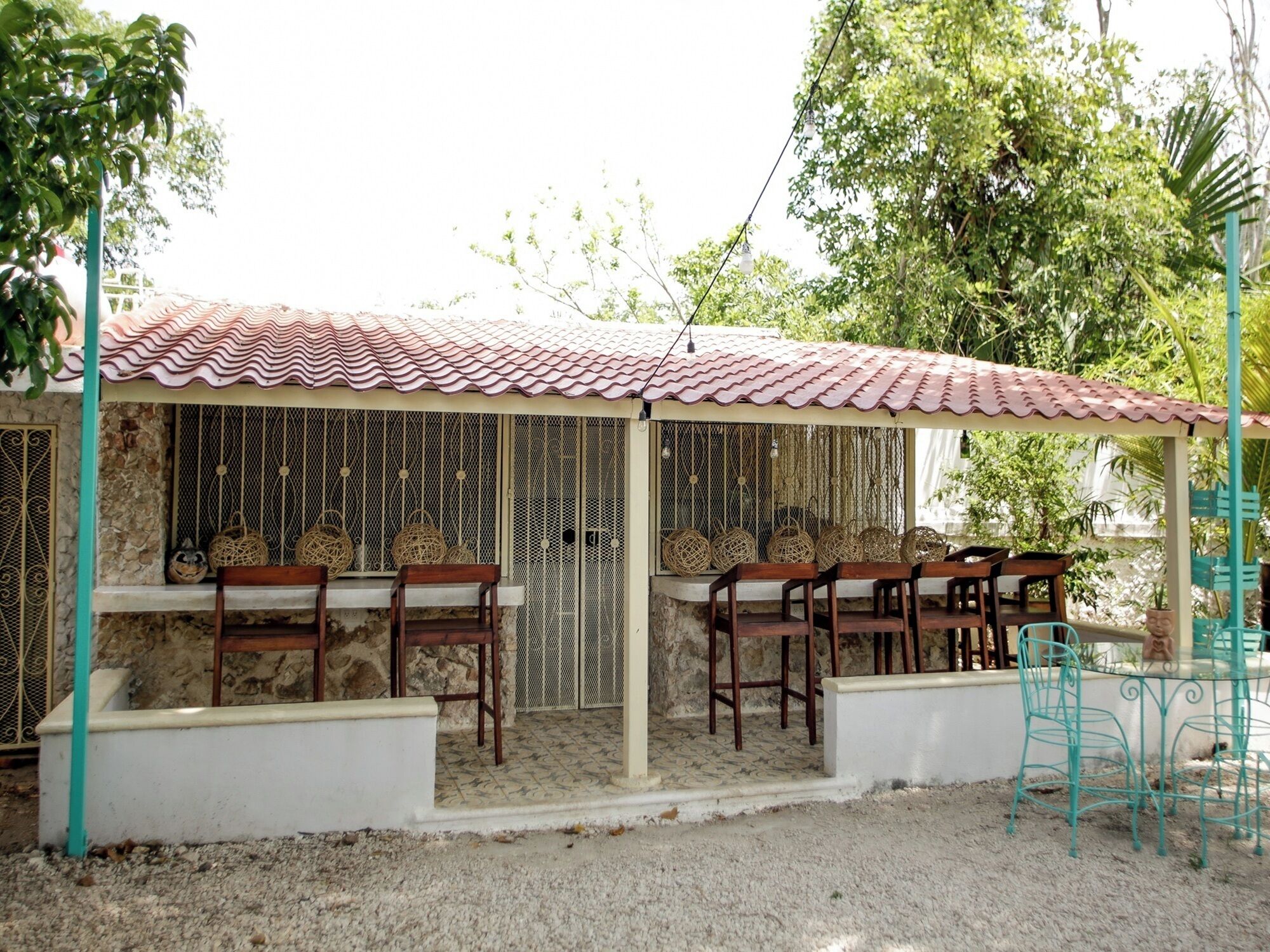 A small outdoor seating area with a tiled roof, stone walls, and metal chairs.