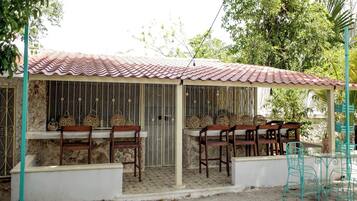A small outdoor seating area with a tiled roof, stone walls, and metal chairs.