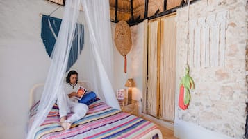 A room with a bed under a white canopy, a stone wall, and a woven wall hanging.