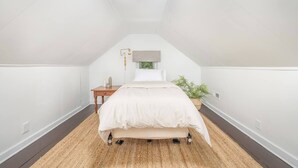 A bedroom with a sloped ceiling, a bed with a white duvet, a bedside table with a lamp, and a potted plant. - Gambier I MountVernon I BikePath (Mount Vernon)