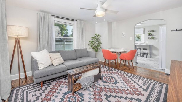 A modern living room with a grey sofa, a coffee table, and a patterned rug. There is a dining area with a small table and orange chairs. - Gambier I MountVernon I BikePath (Mount Vernon)