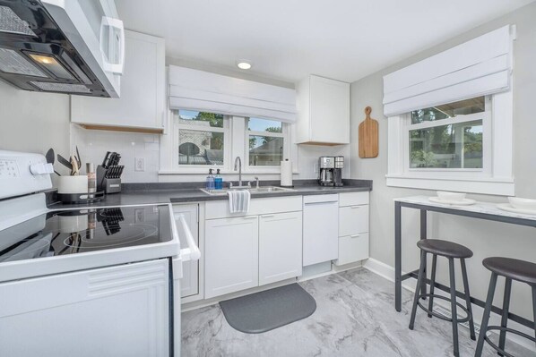 A modern kitchen with white cabinets, a black countertop, a built-in oven, a coffee maker, and a wooden cutting board on the wall.