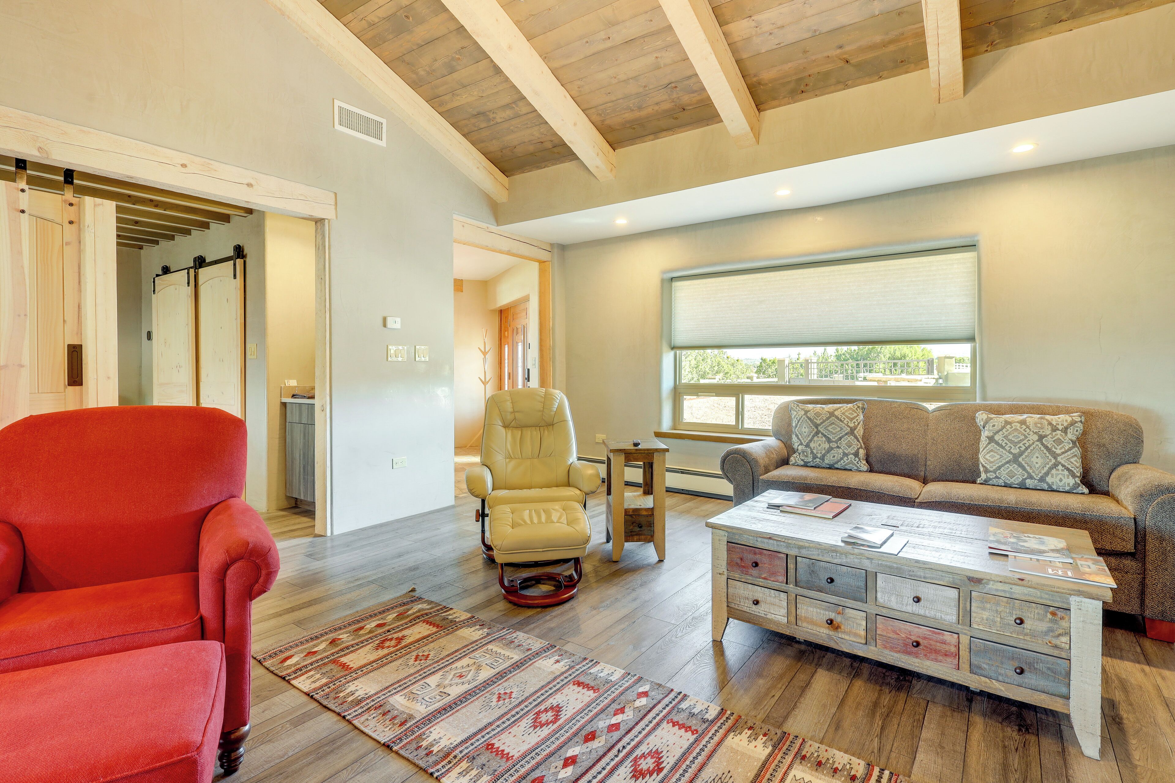 A spacious living room with a red armchair, a beige recliner, a wooden coffee table, and a brown sofa with patterned cushions.
