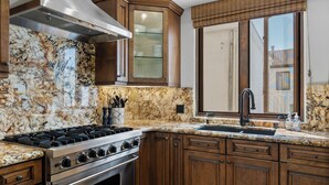A kitchen with a gas stove, oven, wooden cabinets, granite countertop, and a window with blinds. - Luxury Coastal Home with Rooftop Deck & Ocean Views in Newport Beach (Newport Beach)