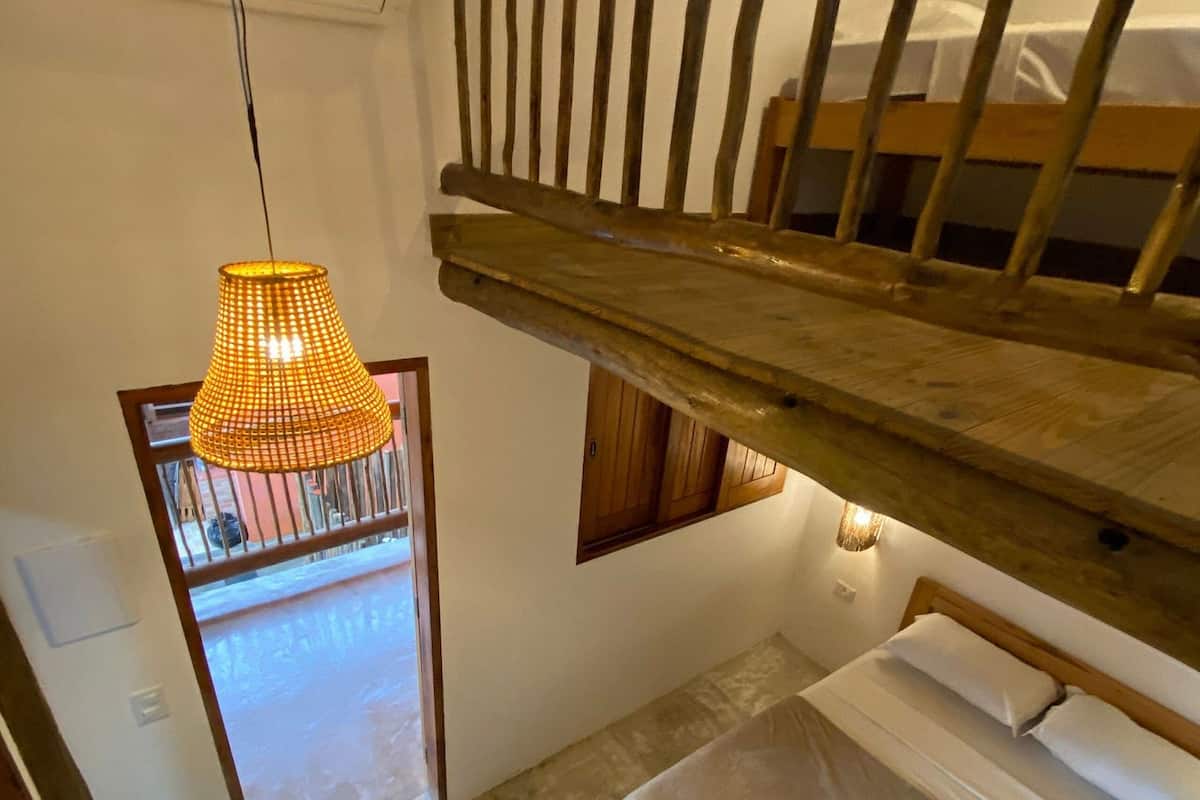 A small, cozy room with a bunk bed, a hanging light fixture, and a view of the outside.