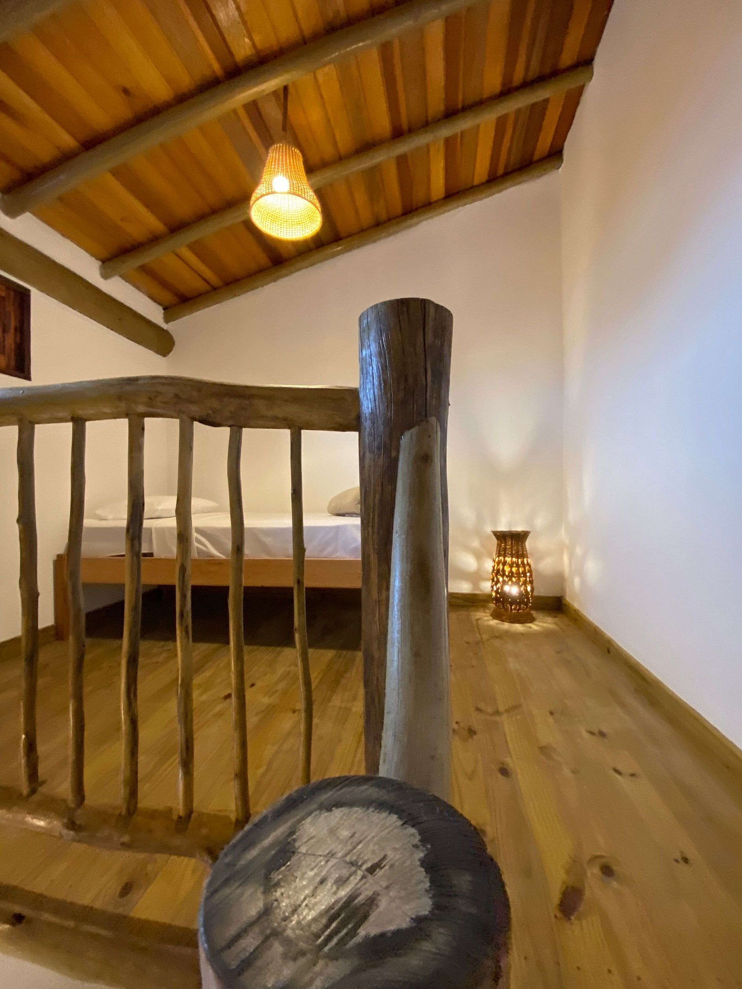 A wooden staircase with a handrail, a bed with white bedding, and a small table with a candle.