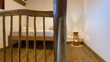 Una escalera de madera con barandilla, una cama con ropa blanca y una mesita con una vela.