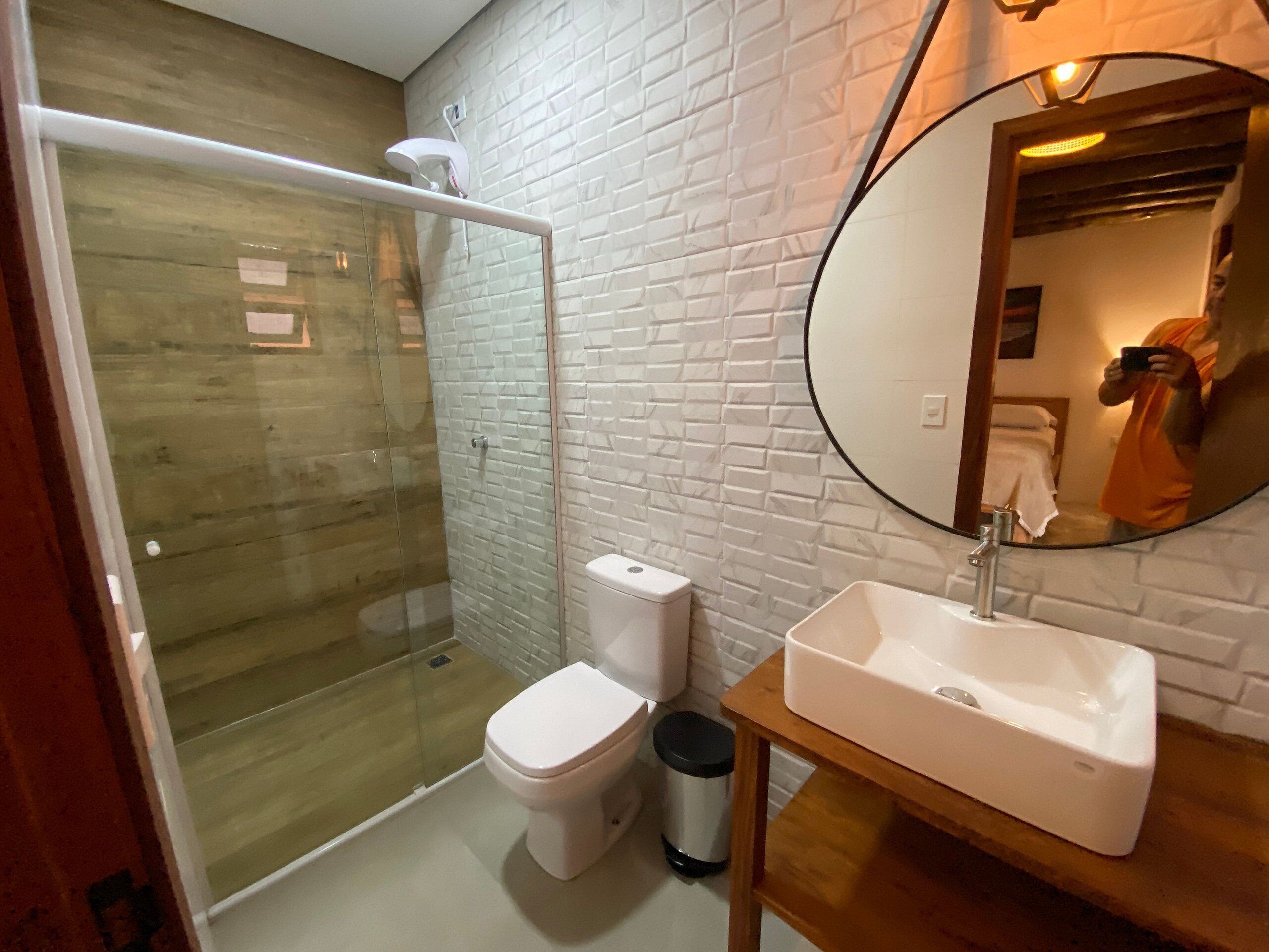 Un baño con ducha envuelta en vidrio, inodoro blanco y lavamanos con espejo.
