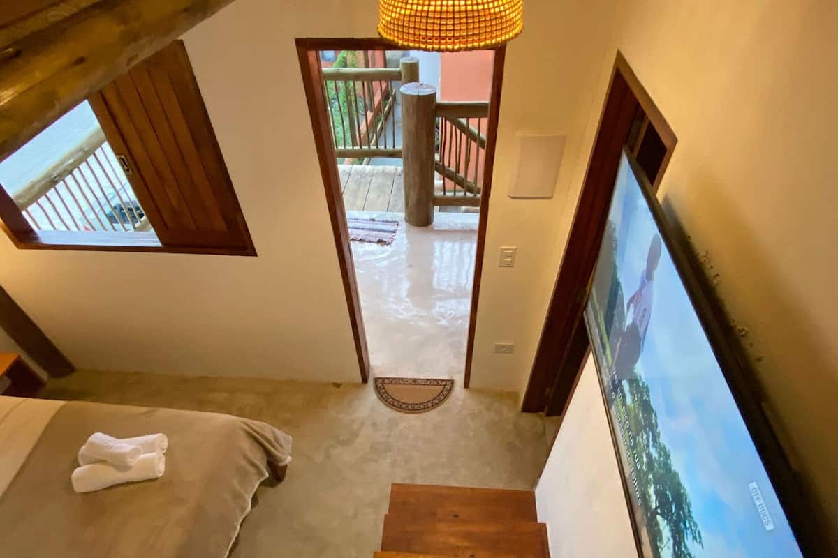 A staircase leading to a bedroom with a bed, a wooden bench, a hanging light fixture, and a TV on the wall.