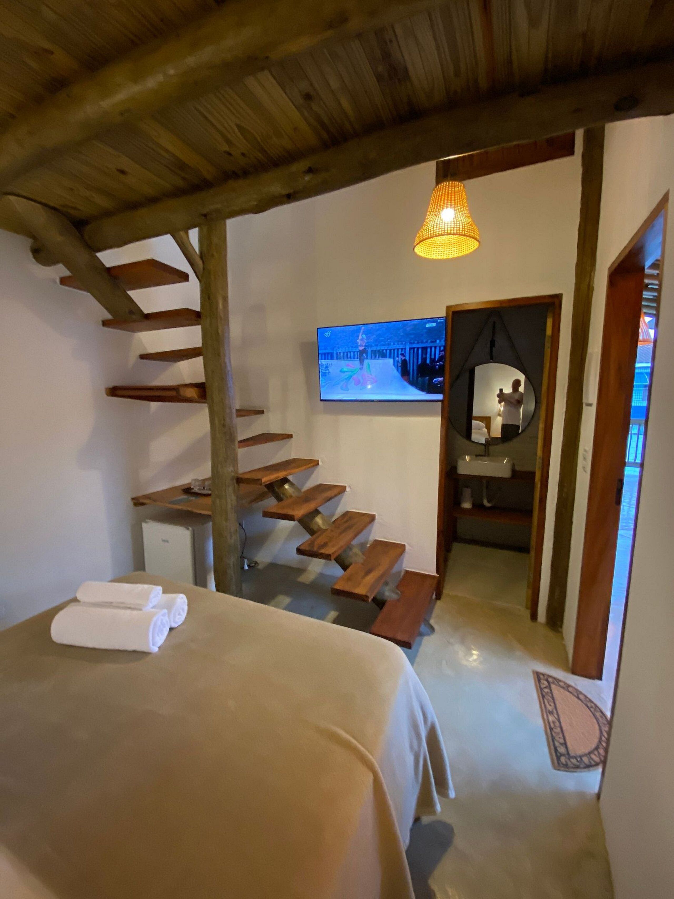 Um quarto com cama, escada de madeira, televisão e espelho.