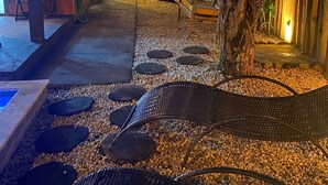 A pathway with stepping stones leading to a seating area, surrounded by tropical plants and a wooden fence. - Lalabella Praia Grande (Ubatuba)