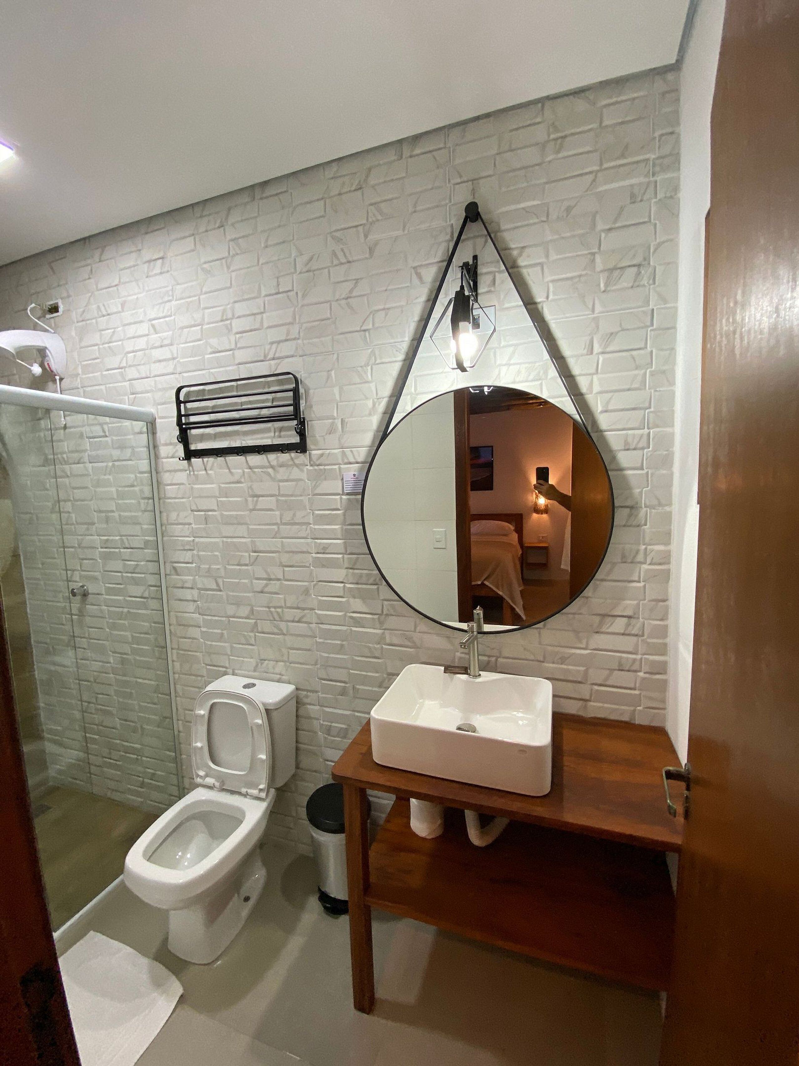 A bathroom with a white brick wall, a round mirror, a white sink, and a toilet.