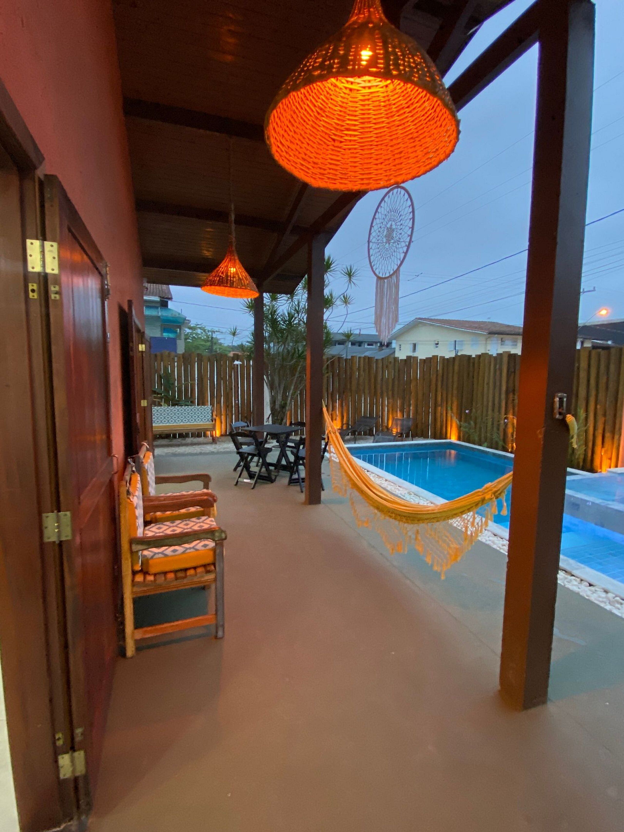 Un patio exterior con piscina, muebles de madera y lámparas naranjas colgantes.