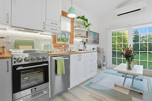 Una cocina moderna con armarios blancos, horno empotrado y comedor con mesa y sillas.