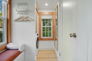 A narrow hallway with a wooden bench, a window with a view of greenery, and a door with a mirror. - Mountain-side modern tiny cabin with fire pit (West Windsor)