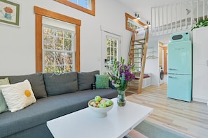 A modern living room with a grey sofa, a white coffee table with a bowl of apples, and a vase with flowers. - Mountain-side modern tiny cabin with fire pit (West Windsor)