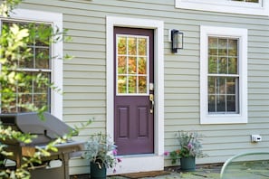 A house with a purple front door, two windows, and a porch with potted plants. - Mountain-side modern tiny cabin with fire pit (West Windsor)