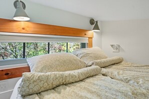 Una cama con ropa de cama estampada, un cabecero de madera, una ventana con persianas y un aplique de pared.