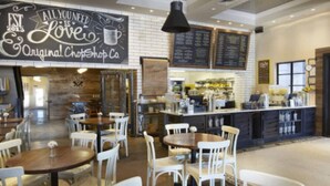 L’intérieur d’un café, avec ses tables et ses chaises, un tableau noir servant de menu et une pancarte sur laquelle on peut lire : « Tout ce dont vous avez besoin, c’est de l’amour. »