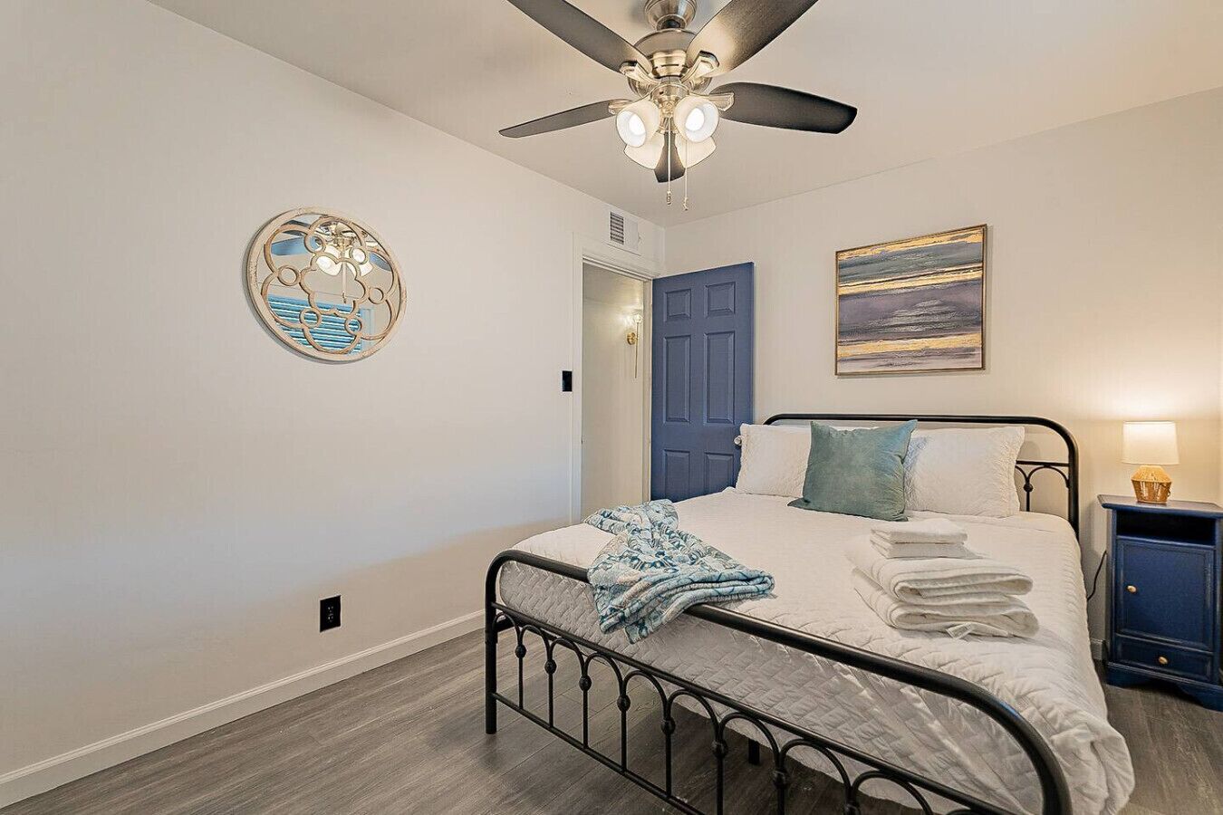 A bedroom with a bed, a ceiling fan, a door, a wall clock, and a painting.