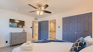 Une chambre à coucher avec un lit, un ventilateur de plafond, une télévision et une commode.