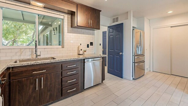 Une cuisine moderne avec des meubles de couleur bois foncé, un lave-vaisselle en acier inoxydable et une porte bleue.