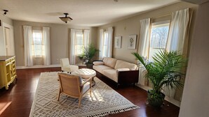 Un salon avec un canapé beige, une table basse ronde, un fauteuil en osier et un meuble jaune.