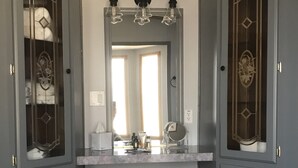 Ein Badezimmer mit zwei Türen, einem Spiegel, einer Lampe und einem Mülleimer.