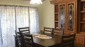 Ein Essbereich mit einem Holztisch, Stühlen, einer Chandelüstere und einem Schrank mit Glastüren.