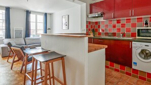 A modern kitchen with red cabinets, a built-in microwave, and a washing machine. - Appartement Garnet - Welkeys (Paris)