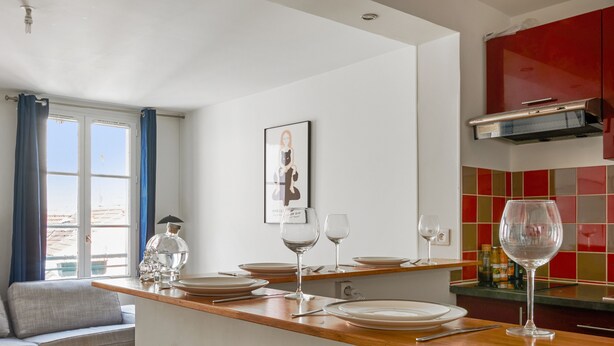 A modern kitchen with a wooden countertop, dining area with a sofa, and a red backsplash. - Appartement Garnet - Welkeys (Paris)