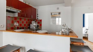 A modern kitchen with red cabinets, a microwave, and a wine glass on the counter. There are three wooden stools at the bar. - Appartement Garnet - Welkeys (Paris)