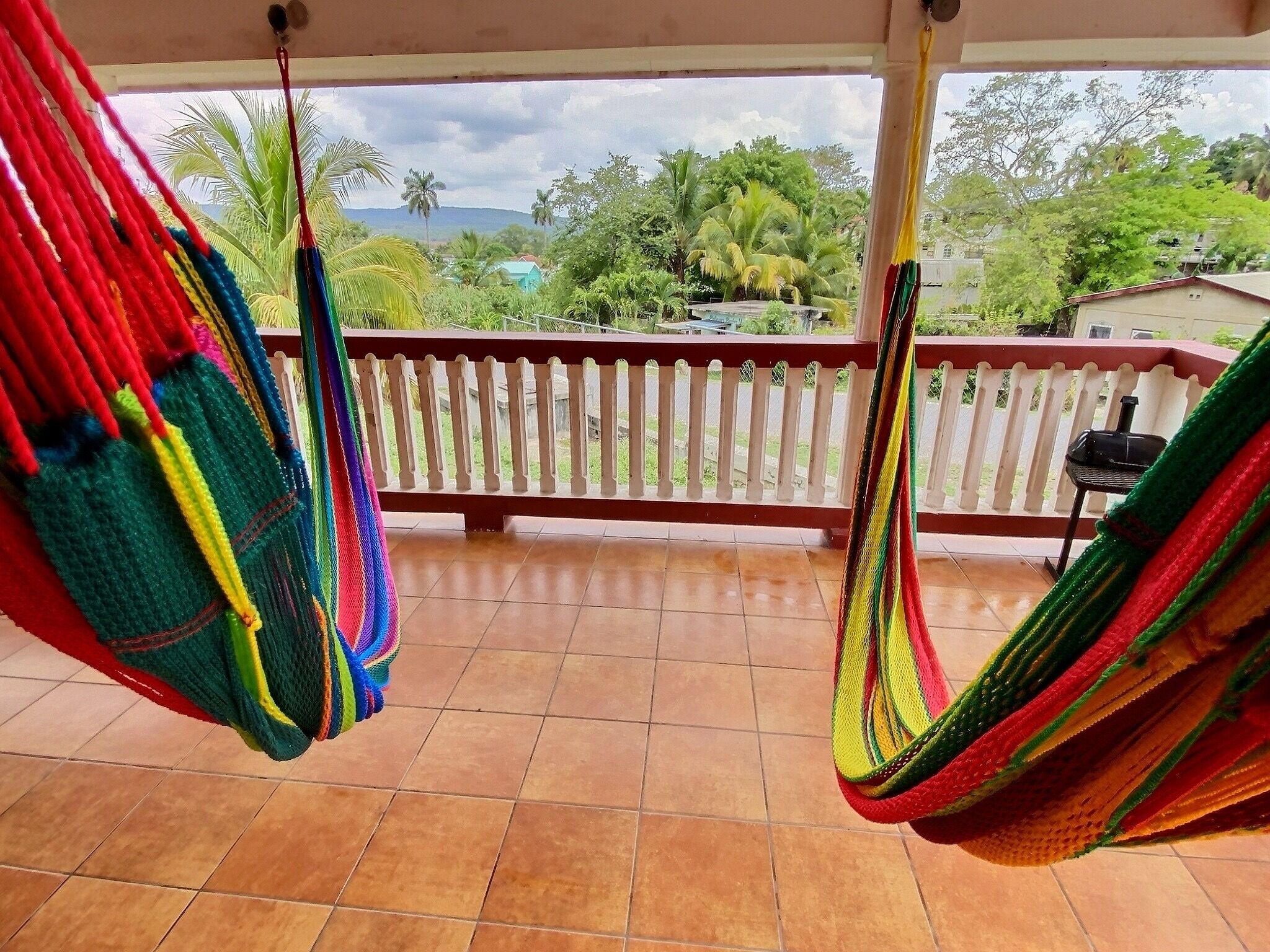 A balcony with two colorful hammocks and a view of a residential area with trees and houses.