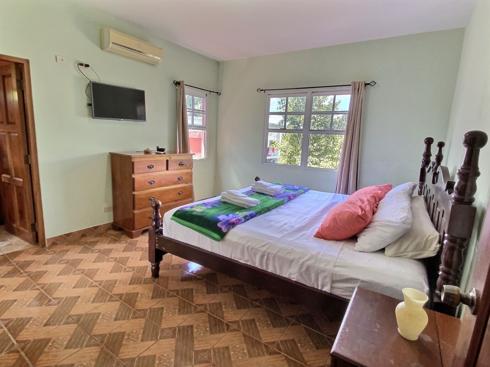 A bedroom with a bed, wooden dresser, and a television on the wall.