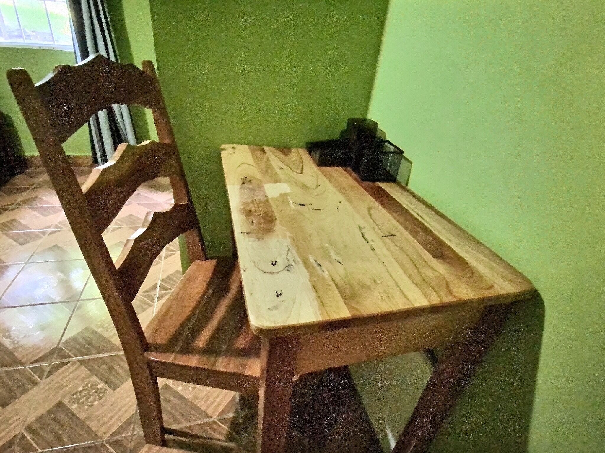 A wooden dining table with a chair, a green wall, and a tiled floor.