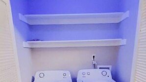 Una lavanderia con due lavatrici bianche a carica frontale e uno scaffale illuminato di blu sopra.