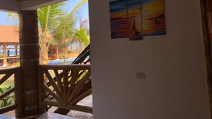 A room with a wooden ceiling, a balcony with a wooden railing, and a view of palm trees and a building outside. - Hosteria de Kade (Manglaralto)