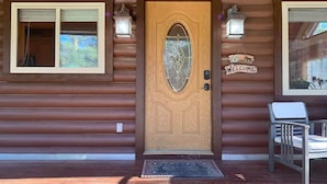 A wooden cabin with a number '3910' above the door, a welcome sign, and a bench outside. - Brevort Log Cabin, Michigan's UP (Moran)