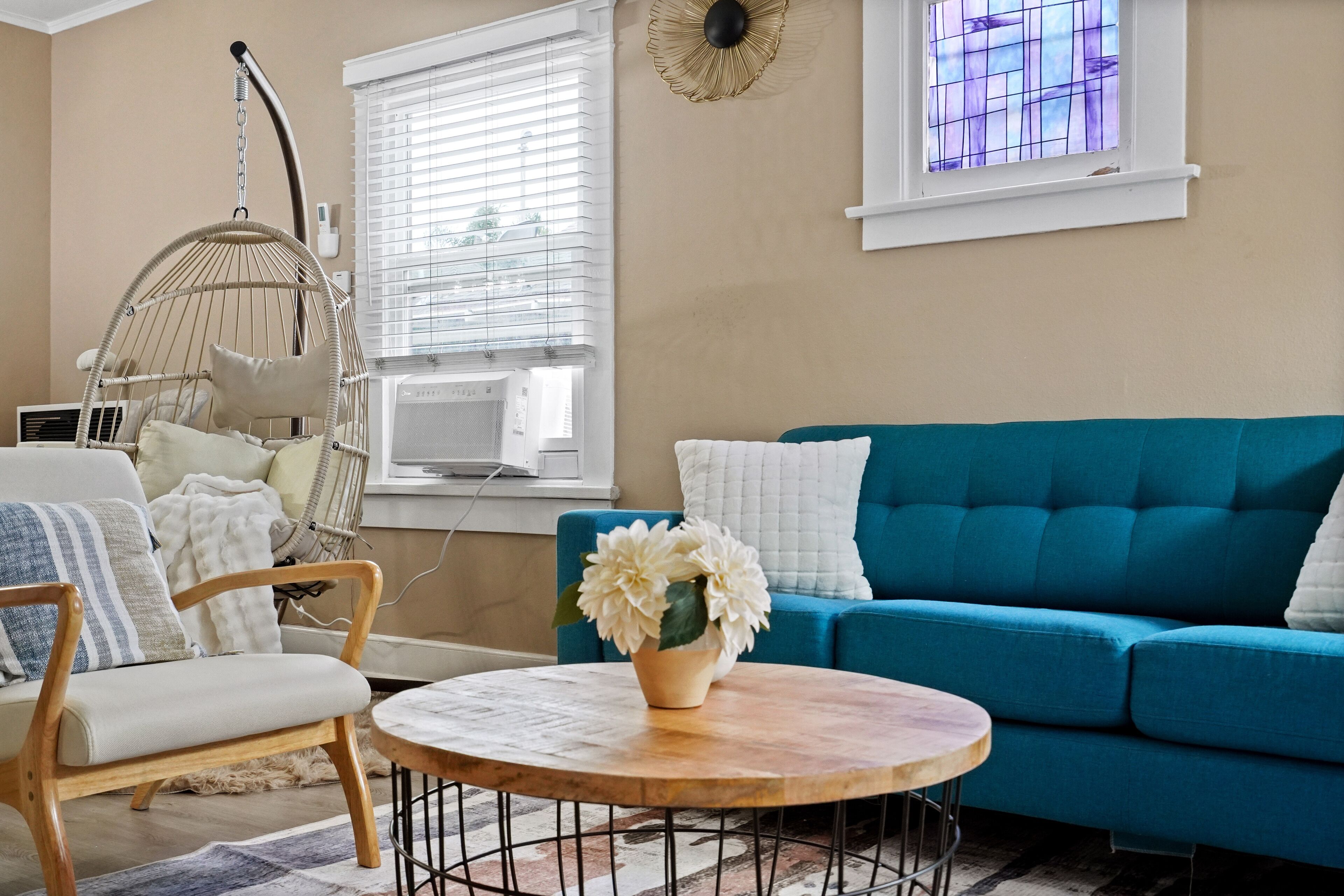 A living room with a blue sofa, a hanging chair, a round wooden coffee table, and a window with blinds.